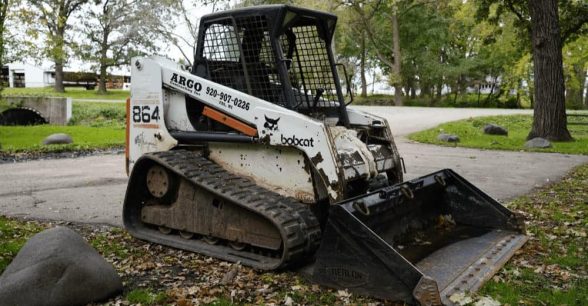 Bobcat Front track Skid loader surrounded by grass and fallen leaves.