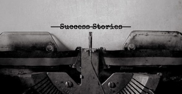 A close-up of a typewriter with a piece of paper in it that says "success stories." The words are crossed out with a black line.