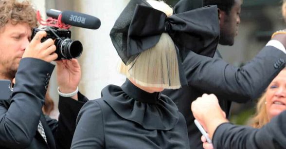 Photo of Sia in a black dress and blonde wig with a black bow.