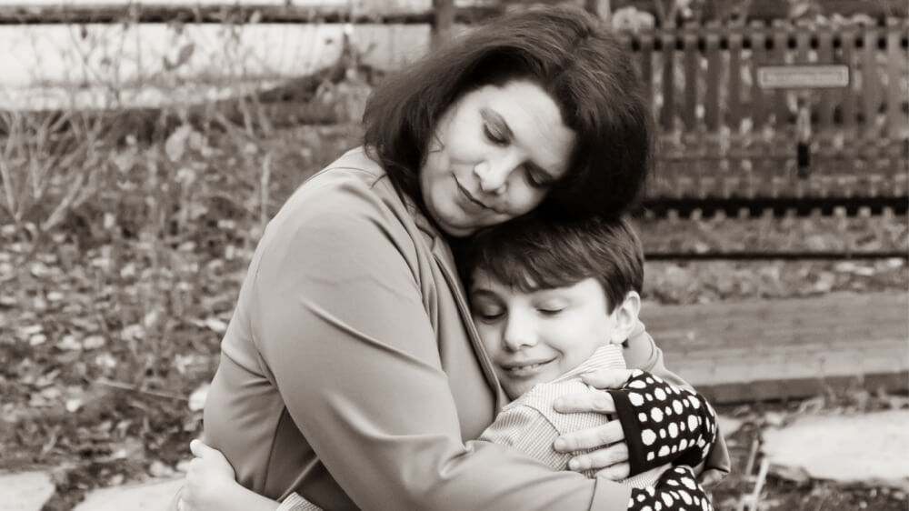 A grayscale photo of the author, a white woman with brown hair just above her shoulder, warmly hugging her son, a young white boy with close cropped brown hair.