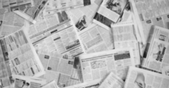 A blurred photo of a scattered pile of newspapers, printed all in black and white.