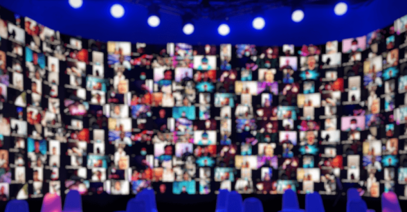 A wide rounded screen of blurred faces, all on webcam, under a row of spotlights.