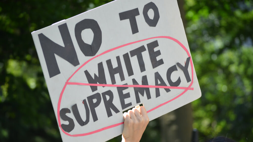 A white person's hand holding up a sign that says "No to white supremacy."
