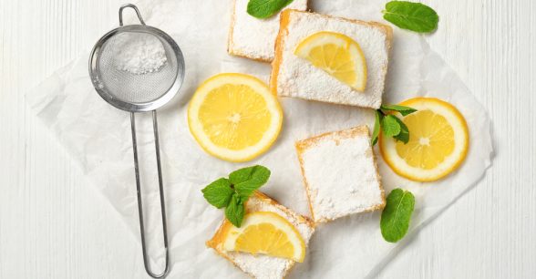 Lemon bars and sieve with powdered sugar on wooden table