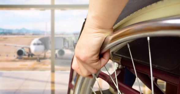 A zoomed-in photo of a person's hand on their wheelchair wheel. They are sitting in front of a window looking out at an airplane.