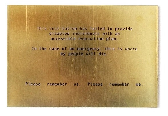 Artwork. A gold plaque has the following written on it in black text: "This institution has failed to provide disabled individuals with an accessible evacuation plan. In the case of an emergency, this is where my people will die. Please remember us. Please remember me."