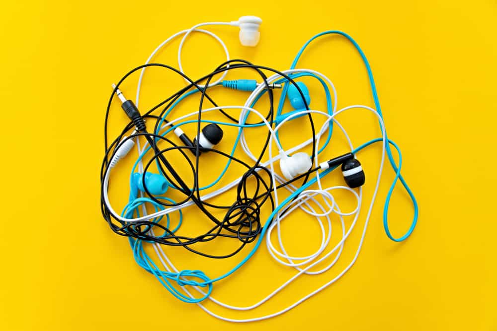 Against a bright yellow background, a small pile of earbud headphones, in different colors, is tangled up together.