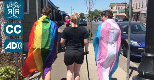 Image of Daisy walking with two friends, Daisy is in the middle of the group. On the back of the person on the left is the gay flag. On the back of the person on the right is the trans flag.