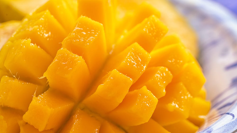 Close up of a ripe, juicy mango that is peeled and sliced to the seed but still attached.