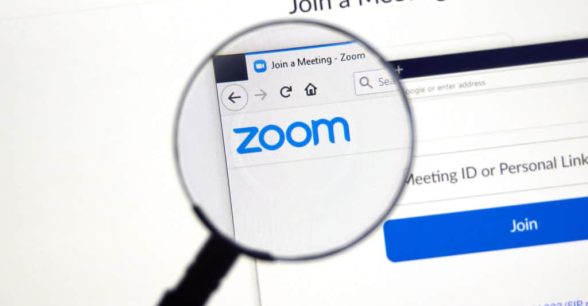 Computer screen with the Zoom logo and a meeting log in page with "Join a Meeting" at the top. A magnifying glass centers on the Zoom logo.