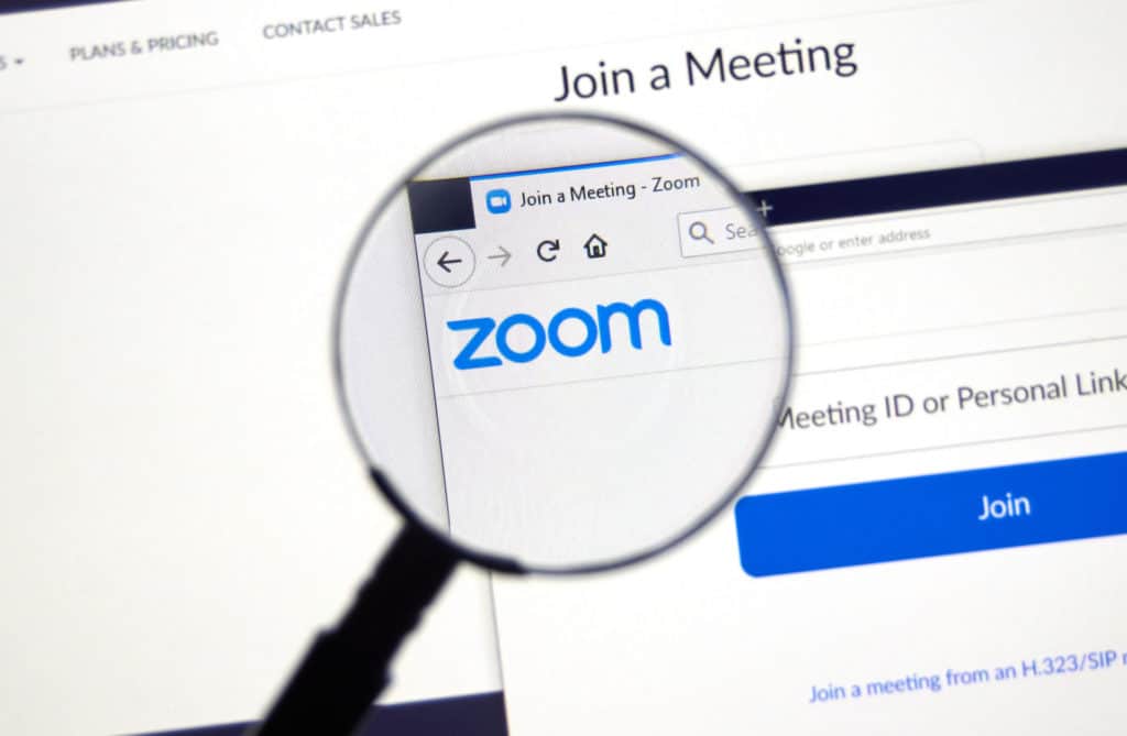 Computer screen with the Zoom logo and a meeting log in page with "Join a Meeting" at the top. A magnifying glass centers on the Zoom logo.