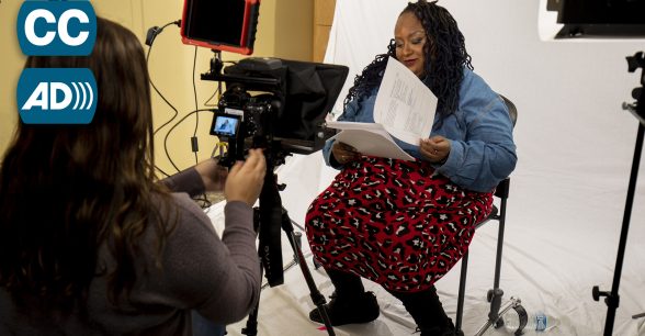 A young Black woman, Imani Barbarin, sits in front of a white backdrop reading a script. A camera, lights and a camera operator point toward Imani.